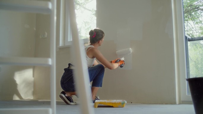 一个女人用滚轴粉刷她梦想中的房子的墙壁。穿防护服