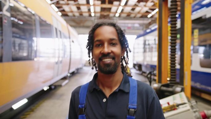 快乐的年轻非洲火车工程师穿着制服走在铁路车间