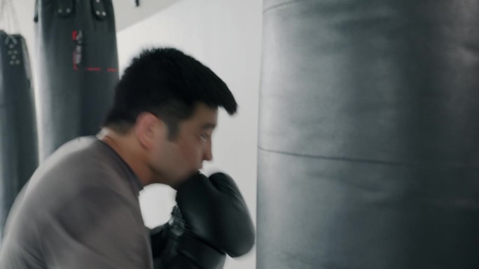 慢动作，强大的亚洲男子训练与拳击袋殴打它与拳击手套在健身房锻炼