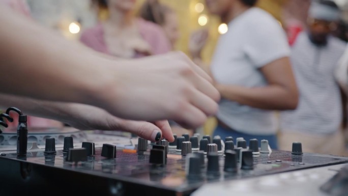 在户外咖啡馆里，当一群人跳舞享受派对时，手DJ混合音乐的特写