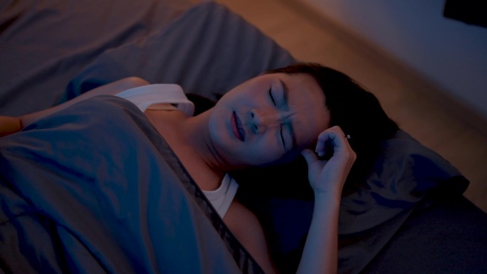 一个亚洲女人晚上躺在床上头痛。