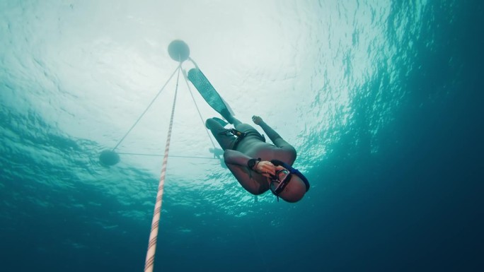自由潜水者沿着绳索下降。一名女子自由潜水者在开阔的海面上沿着绳子游到深处