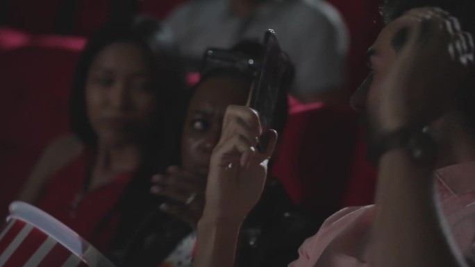 年轻的拉美裔男子在电影院看电影时用智能手机打电话，打扰了观众。电影放映期间禁止打电话。一个男人在剧院