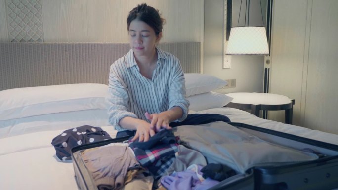 亚洲女人带着装衣服的箱子
在酒店房间里，为一个轻松的独自旅行度假或新的冒险准备行李。