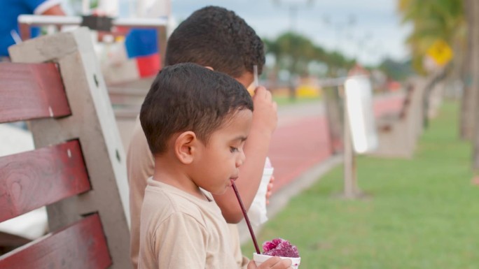 拉丁裔孩子坐在长凳上喝着树莓葡萄。搭配卡其色毛衣