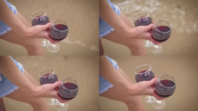 女人手里拿着两杯红酒，靠近海浪的背景