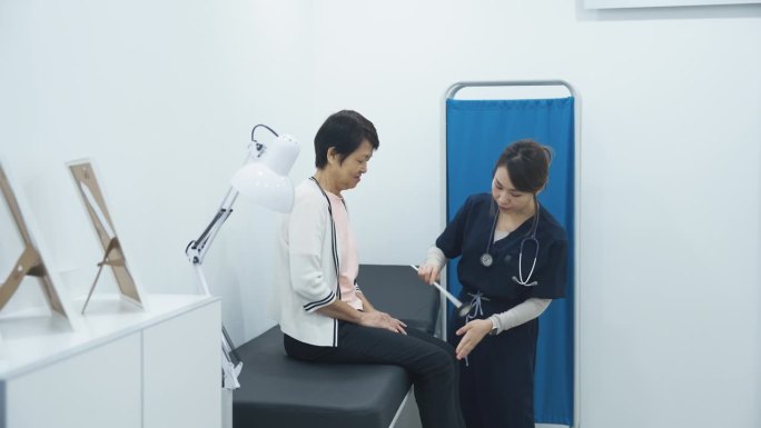 亚洲华裔女医生在门诊诊室用反射锤敲打老年妇女膝盖检查神经系统