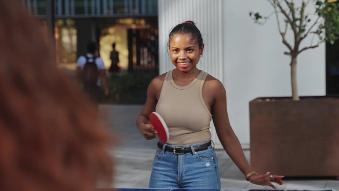 非裔美国女孩和学生朋友打乒乓球，在大学里玩得很开心