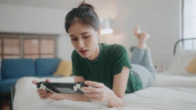 休闲玩家:微笑的年轻女性在现代卧室用电子游戏拥抱快乐和休闲。