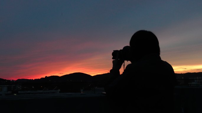 日落时在楼顶的摄影师拍照和夕阳说再见挥手