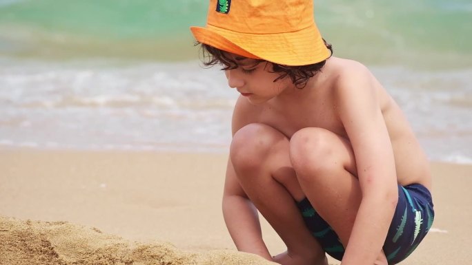 一个男孩在沙滩上玩沙子。孩子堆沙堡特写。
