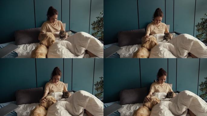 一个黑发女孩躺在床上，旁边是她的狗和猫。猫不喜欢狗的存在，但女孩调和了它们。在家与宠物互动