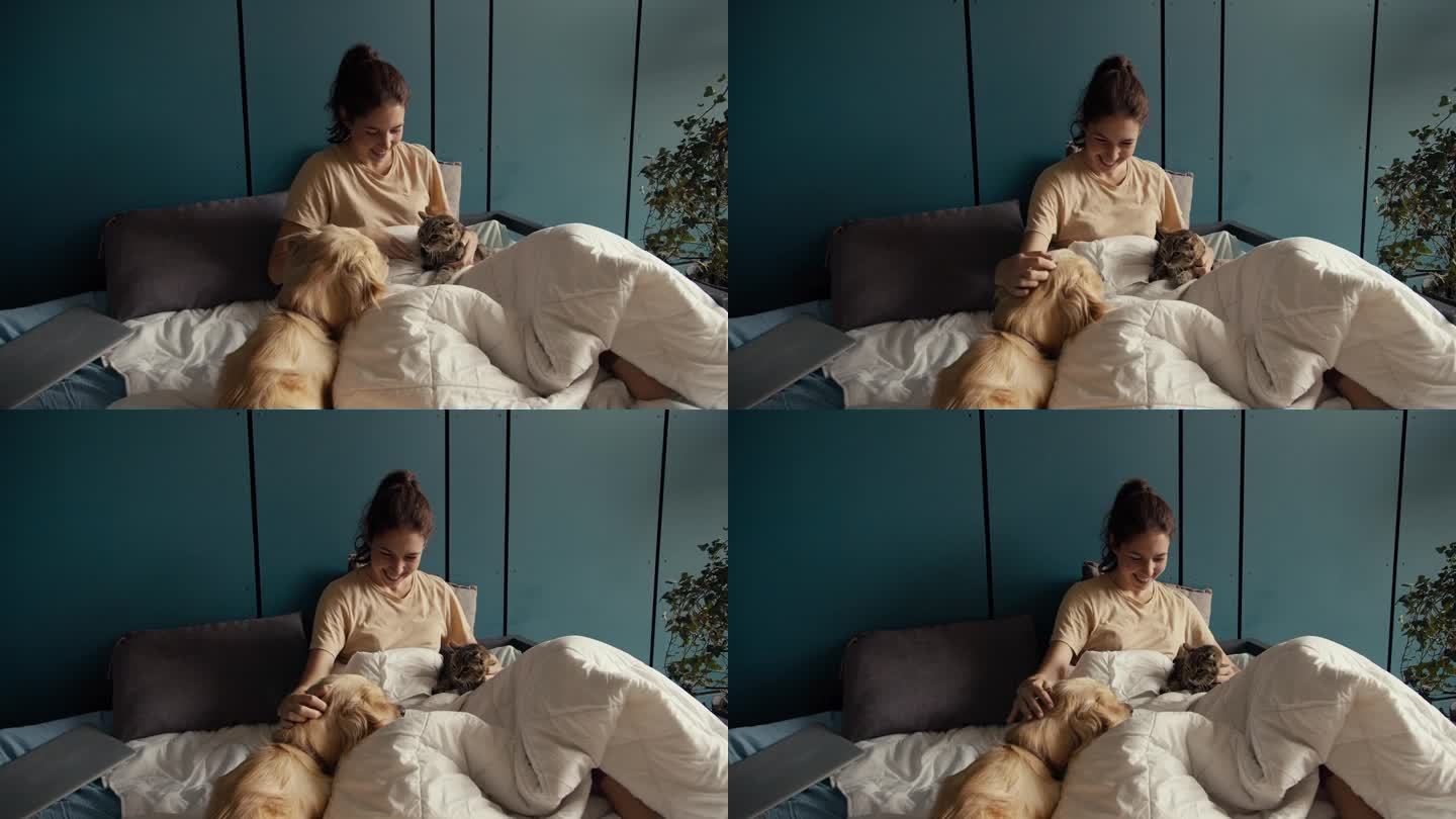 一个黑发女孩躺在床上，旁边是她的狗和猫。猫不喜欢狗的存在，但女孩调和了它们。在家与宠物互动