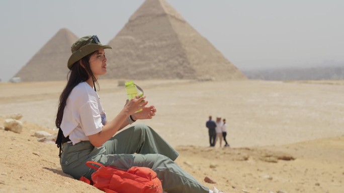 埃及，开罗，亚洲女游客坐在岩石上，背景是吉萨大金字塔