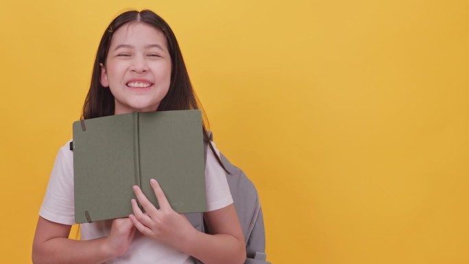 可爱的女学生背着书包，手里拿着一本黄色背景的笔记本。