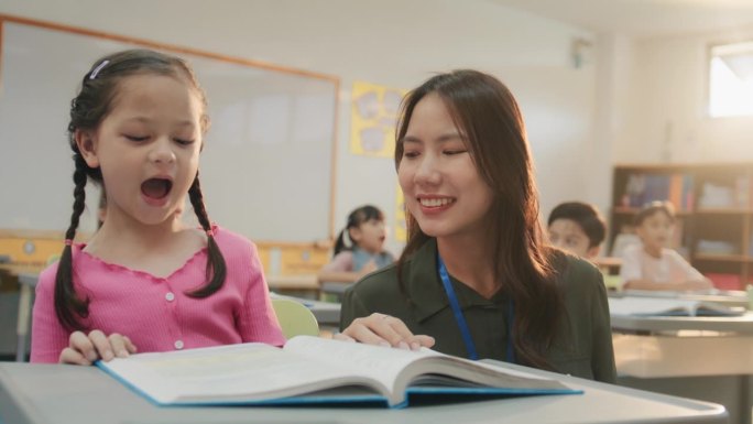 快乐的亚洲小学老师在学校与孩子们一起阅读。