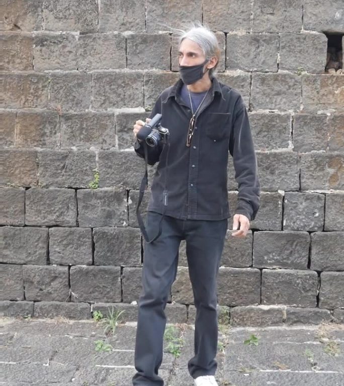 男视频博主拿着相机在石头背景下行走