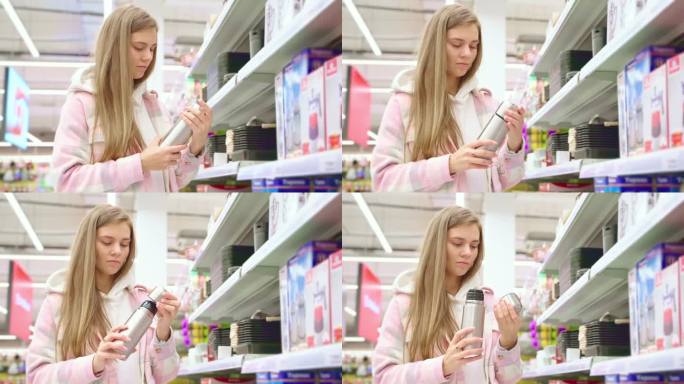 感兴趣的年轻女子在超市橱窗旁挑选保温瓶。