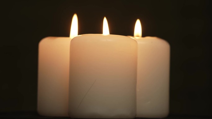 三个白色的石蜡蜡烛与黄色阴影燃烧和旋转在黑色的背景
