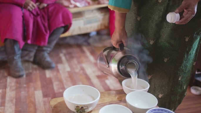 蒙古包里的蒙古妇女为她的丈夫和客人倒奶茶