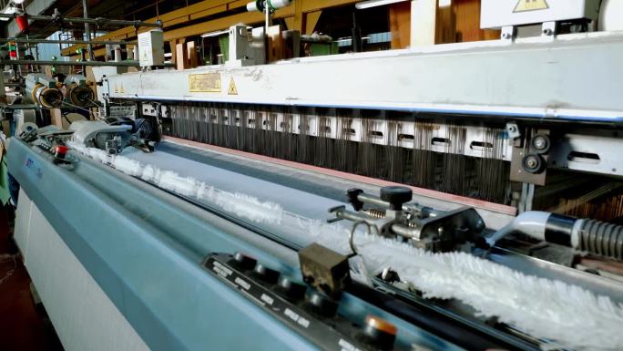 编织织机。纺织工厂。纺织工业。特写镜头。自动织布机正在织造线布。纺织厂设备。面料生产。