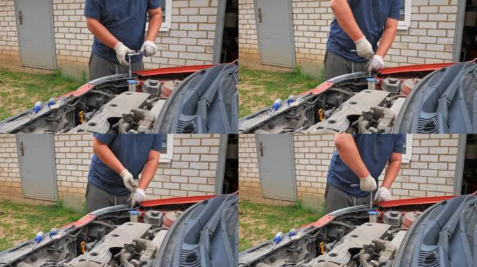 一个男人正在他家院子里的车库附近修理他的汽车。一名男子用扳手拧下螺栓，更换汽车上坏了的部件。汽车修理