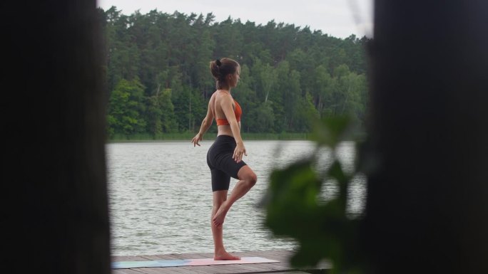 在湖边运动的女人。在木码头上做瑜伽冥想练习
