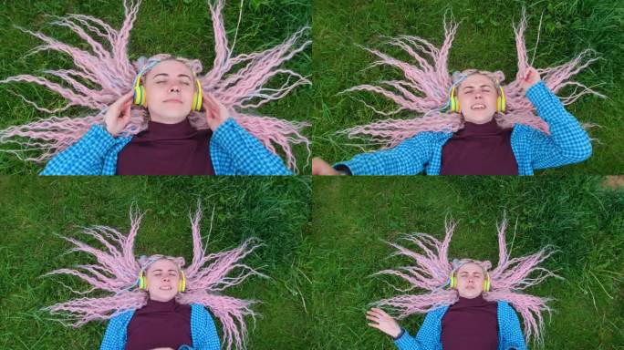 夏天，一个粉红头发的女孩在草地上戴着耳机听音乐