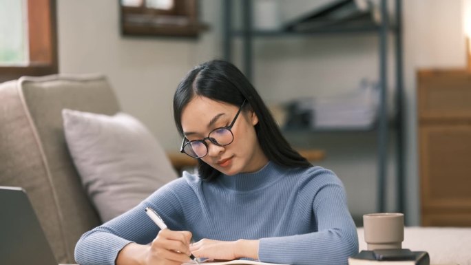 年轻的成年亚洲女学生在家里用笔记本电脑做笔记。亚洲女性在线学习听力虚拟视频通话。商业和教育理念。