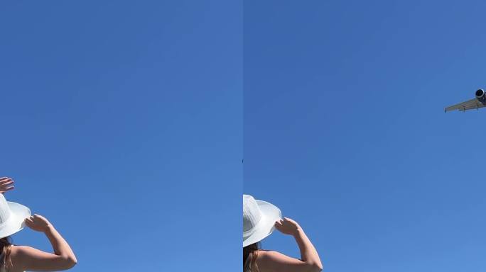 一位戴着白色帽子、身穿白色长裙的游客向一架飞向他的飞机挥手。在女孩的旁边有一个巨大的蓝色手提箱，颜色