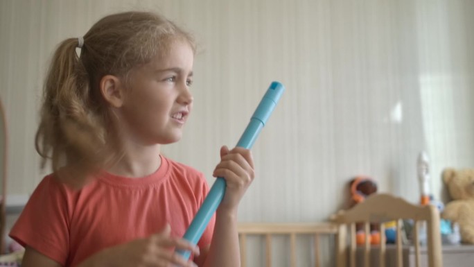 小趣味创意女孩用扫帚柄做麦克风唱歌。小孩在家庭房间唱歌时用拖把当麦克风。享受春季大扫除。顽皮的创意孩