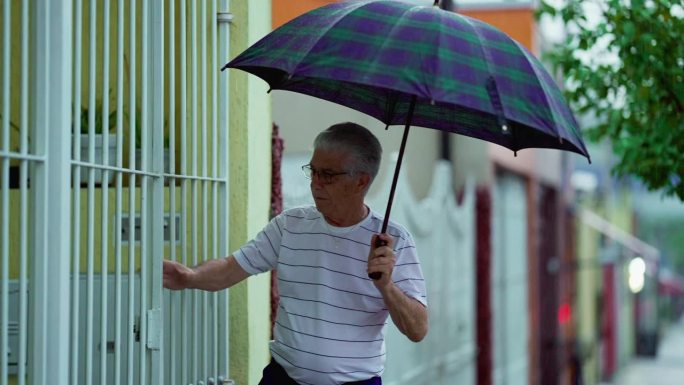 老人在下雨时出门，打开雨伞，关上身后的门。老人走在街道的人行道上