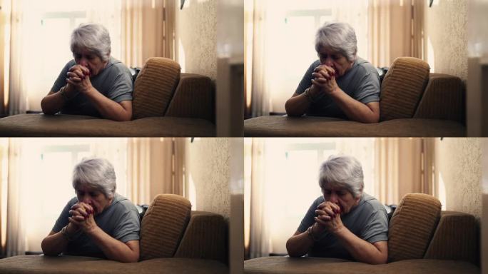 真实的白种老年女性在家祈祷，紧握双手坐在沙发上的老人，奉献与信仰的缩影