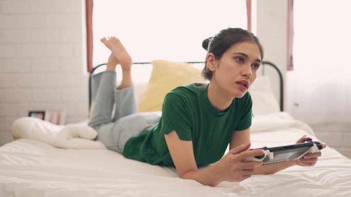 快乐与放松:年轻女性在卧室的床上玩电子游戏时微笑