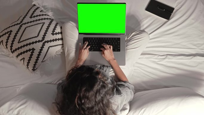 女人工作在笔记本电脑模拟绿屏色度键和键盘上输入文本特写。人坐在床上上网聊天或写文件特写。程序代码或邮