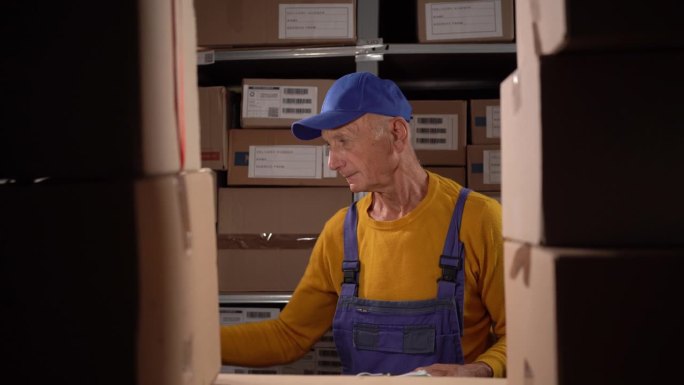 拿着剪贴板的老人在仓库工作。主管控制货物的验收。老男主管进行仓库审核。