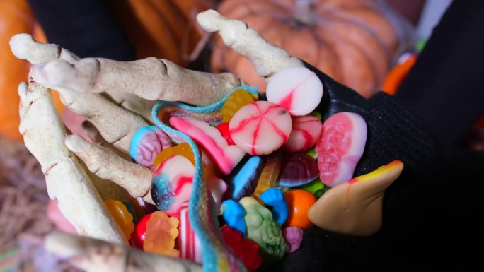 近距离吓人的骷髅手收集山的彩色糖果，糖果，果冻，果酱。