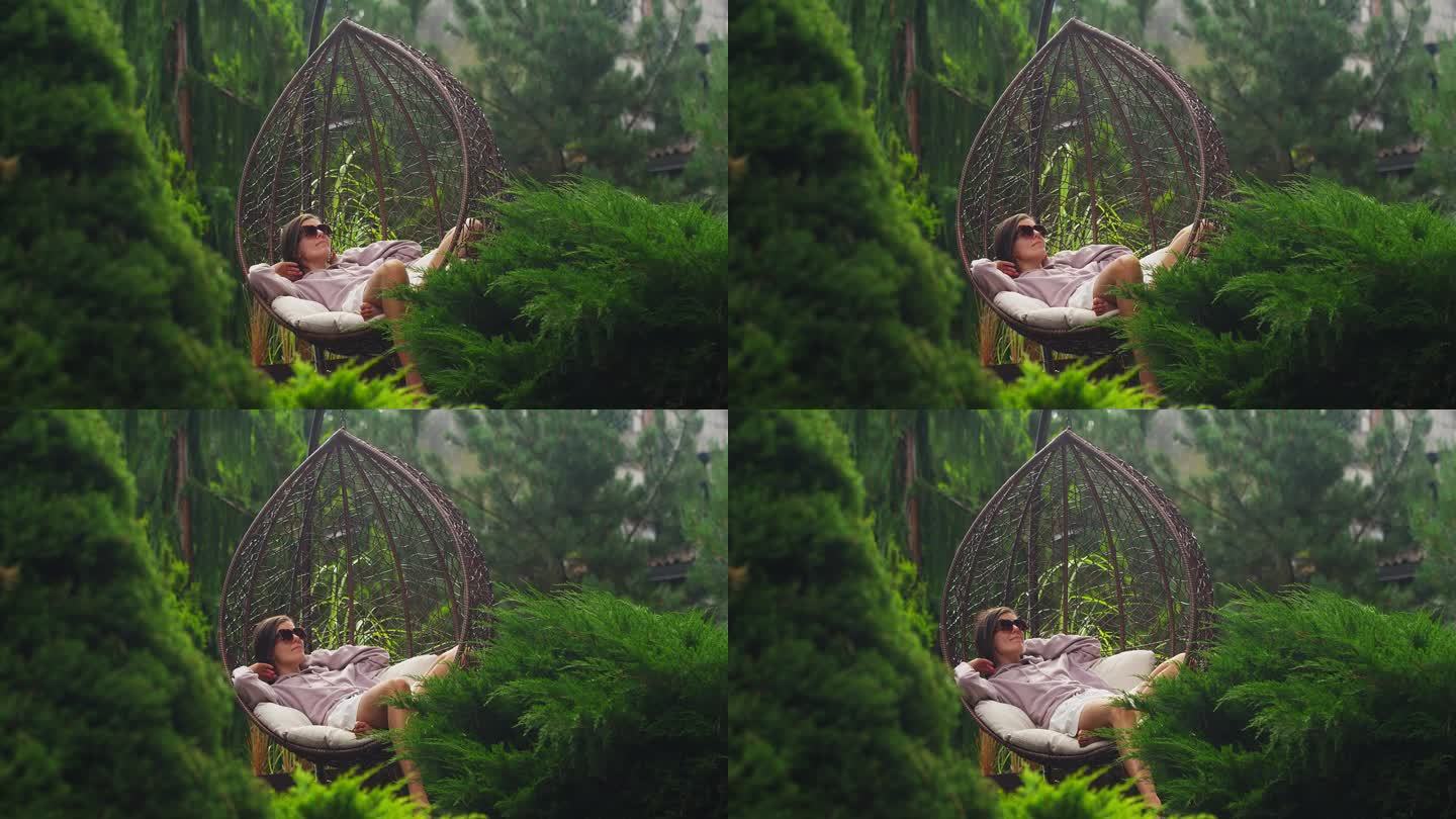 坐在藤椅上的女人。在绿色的花园里放松，享受大自然
