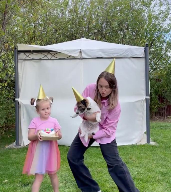 可爱的小女孩和十几岁的女孩在家里的花园里用一个生日蛋糕祝贺她的宠物杰克罗素梗狗。节日庆祝概念。给狗的