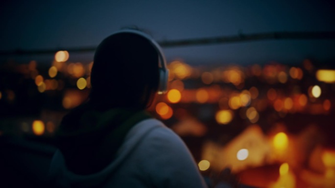 晚上戴着耳机在城市屋顶上听音乐的快乐女人