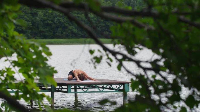 在湖边运动的女人。在木码头上做瑜伽伸展运动