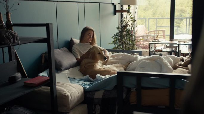 金发女孩和她的狗躺在床上，抚摸着它。与你的宠物和睦相处