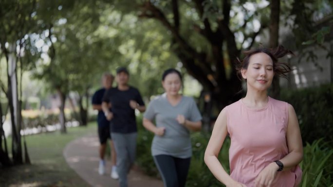 在一个温暖的日子里，女儿妈妈、爸爸和儿子在公园里慢跑的慢动作广角跟踪镜头。