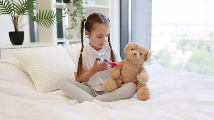 微笑的女孩用床上的玩具注射器给泰迪熊注射疫苗