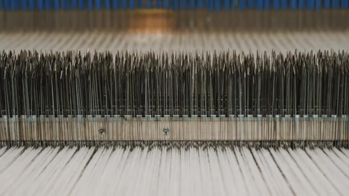 纺织工厂。编织。自动织布机工作中的零件特写镜头。纺织厂设备。工业机器正在释放梭织织物。