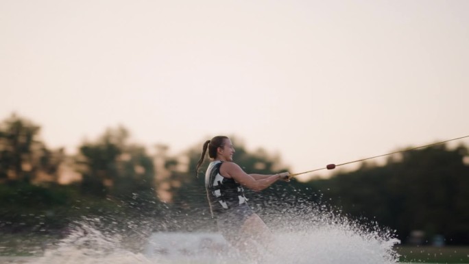 日落时分的女子滑水板运动员。女孩骑在滑水索上。握住牵引绳。夏天在湖里活动。120fps电影摄影机。