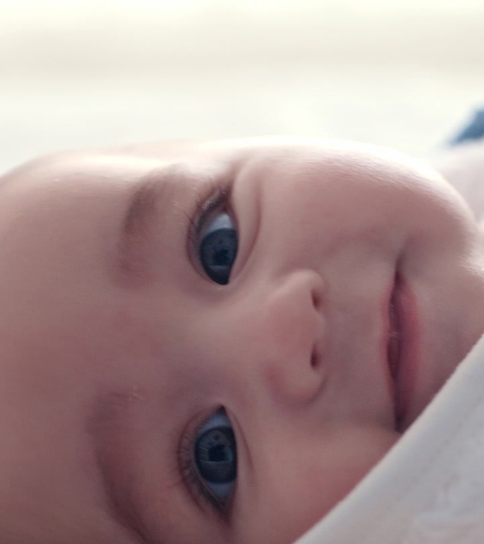 脸，特写和一个微笑的婴儿躺在床上放松，舒适或在早上醒来。快乐，青春和一个新生儿的肖像，孩子或人类在一
