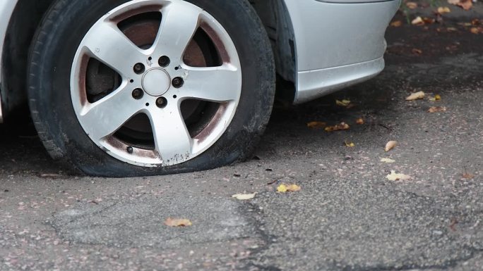 一辆银色轿车前爆胎的特写镜头。坏了的车停在街上。