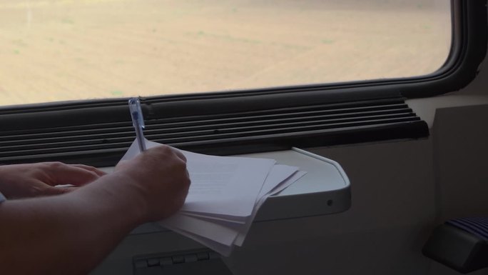 乘客在火车车厢用钢笔在纸上写字的4K镜头，背景是乡村风景。