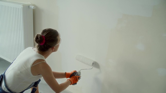 年轻女子用滚轴粉刷她梦想中的房子墙壁。戴护目镜